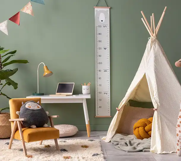 Kinderkamer met een speelwigwam, bureau, knuffels en een groeimeter op een groene muur.
